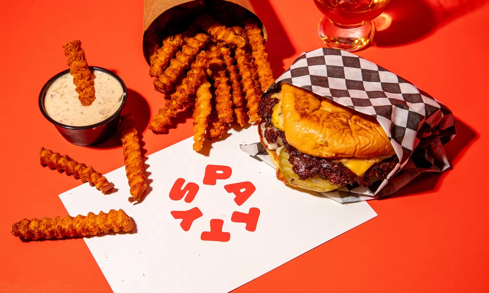 Cheeseburger, crinkle fries with dipping sauce, and a drink on an orange background with a card saying Pattys.