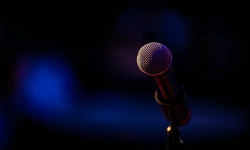 Close-up of a stage microphone with dark blurred background and purple-blue lighting effect.