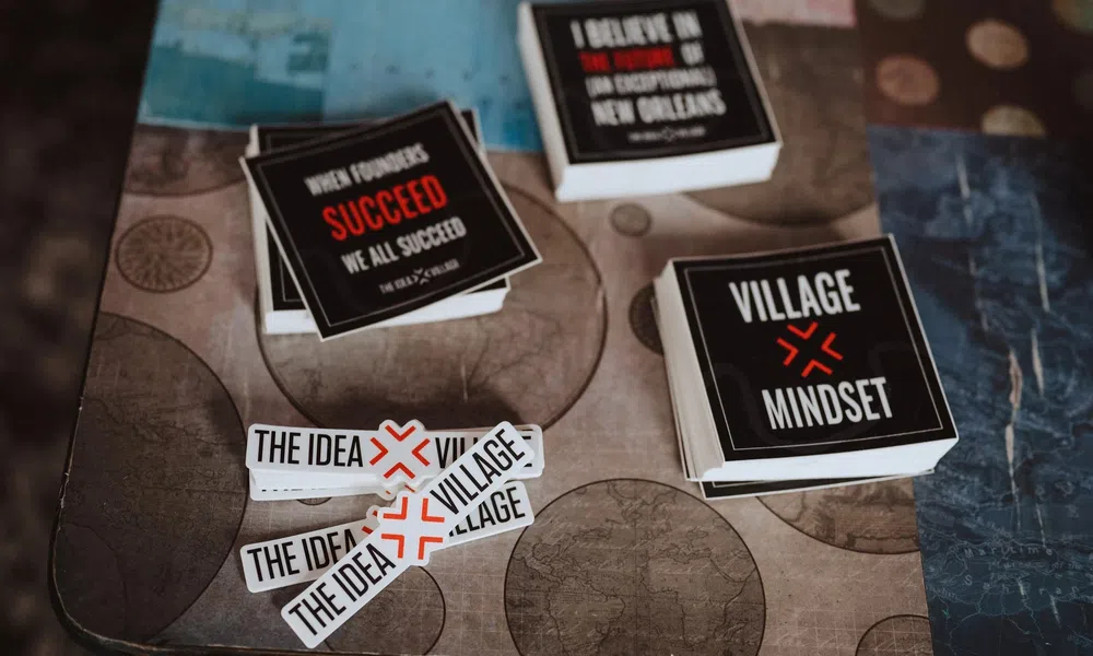 Stacks of motivational and branding stickers on a table featuring phrases like Village Mindset and The Idea Village.