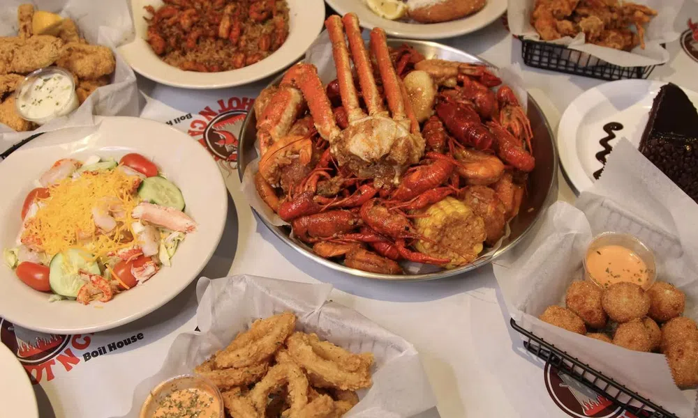 Seafood feast with crab, crawfish, fried shrimp, hush puppies, salad, and dessert on a white table.