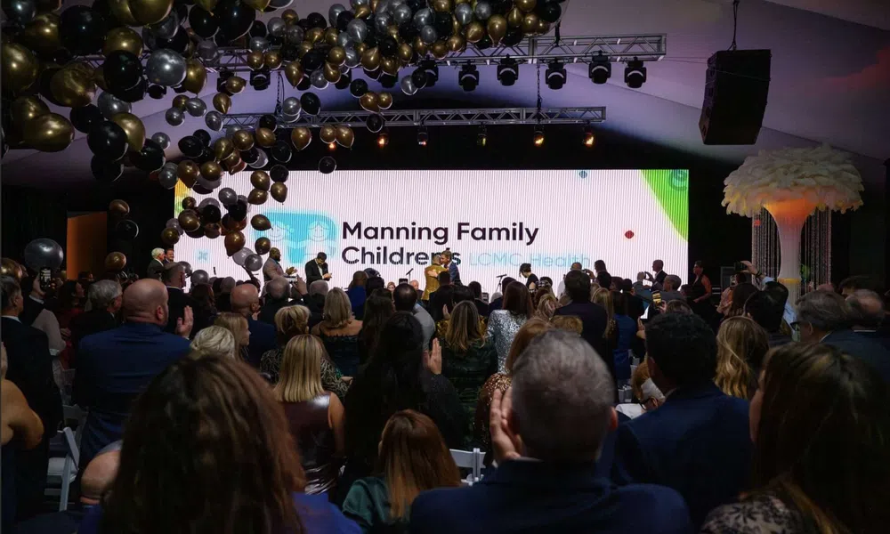 Audience applauding at a formal event with a large screen displaying Manning Family Children's LCMC Health