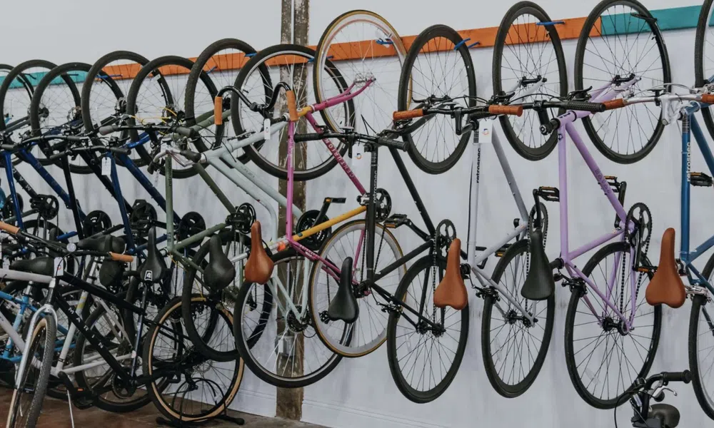 Multiple bicycles with leather seats hanging on wall racks and others parked on the floor in a bike shop.
