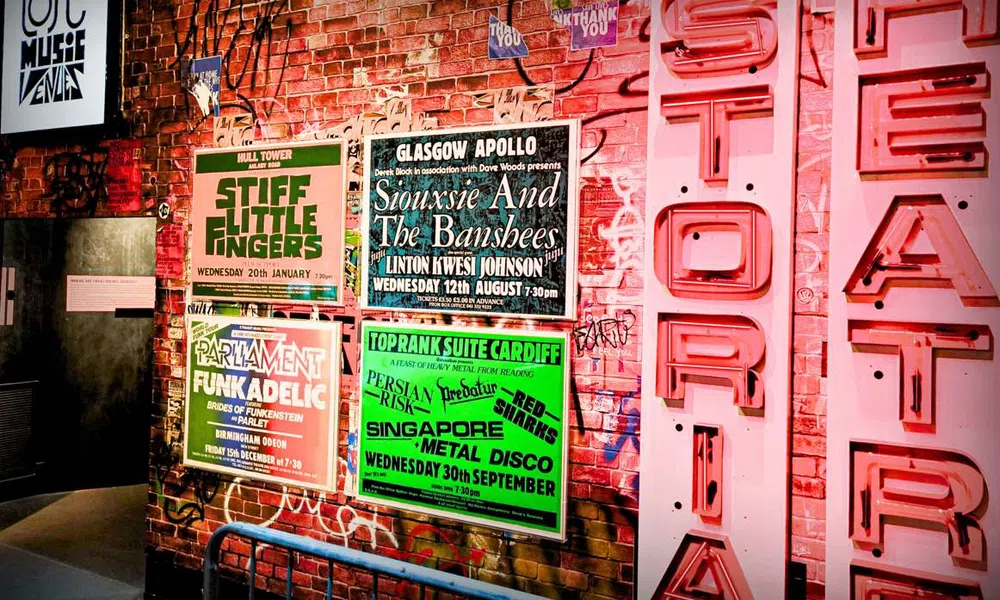 Graffiti-covered brick wall with vintage concert posters and neon Hysteria Theatre sign in a music venue.