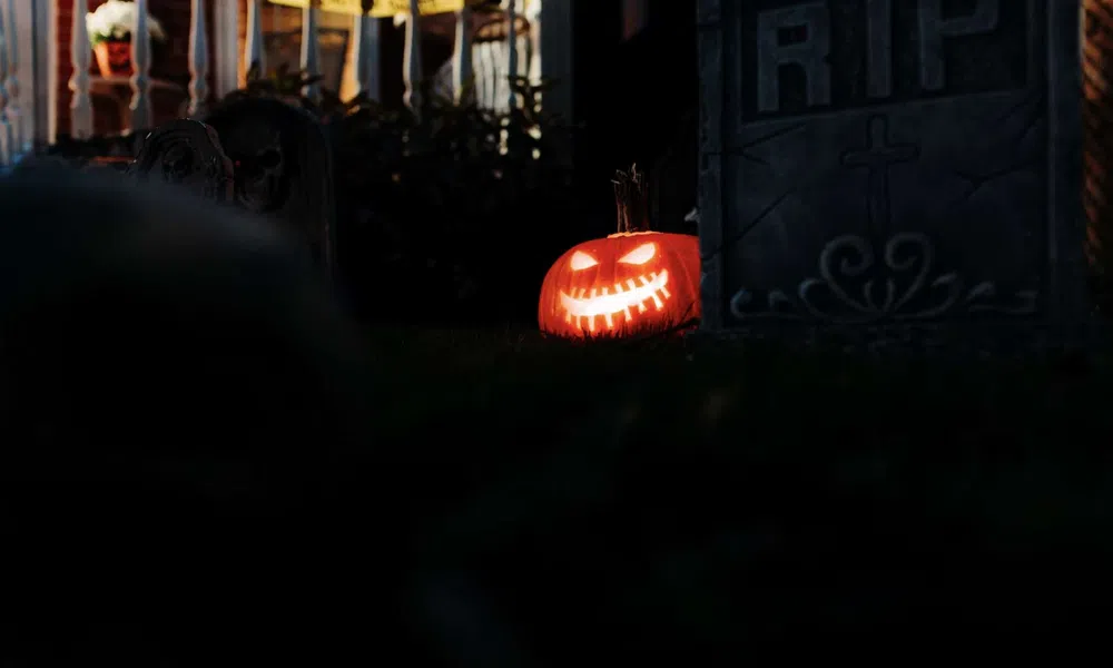 Glowing carved jack-o'-lantern beside a tombstone with RIP in a dark Halloween yard scene.