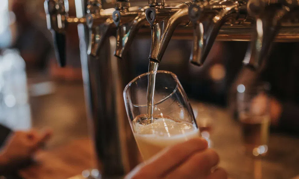 Beer being poured from a tap into a tilted glass at a bar with blurred background.