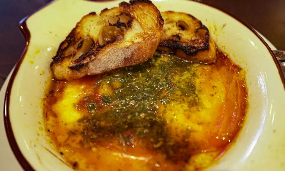 Baked melted cheese with herbs and oil served with crispy toasted bread slices in a rustic dish.