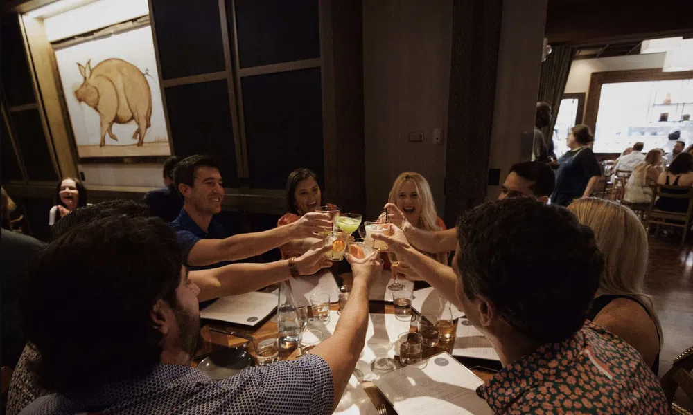 Group of friends raising glasses for a toast around a restaurant table with menus and drinks.