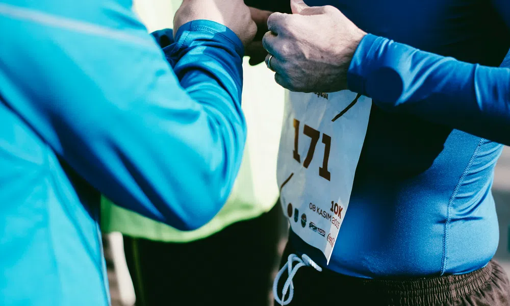 Runners adjusting race bib number 171 before a 10k event on a sunny day with blue athletic gear.