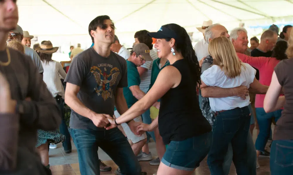 Couples dancing energetically in a lively indoor social dance event under a white tent