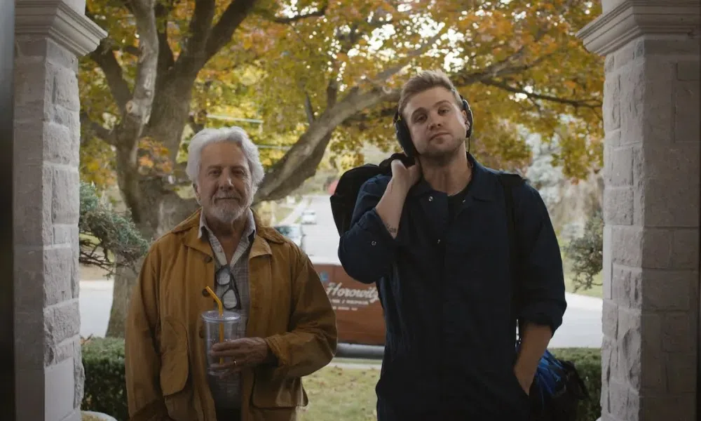 Older man with drink and younger man with headphones and backpack standing on porch in autumn setting
