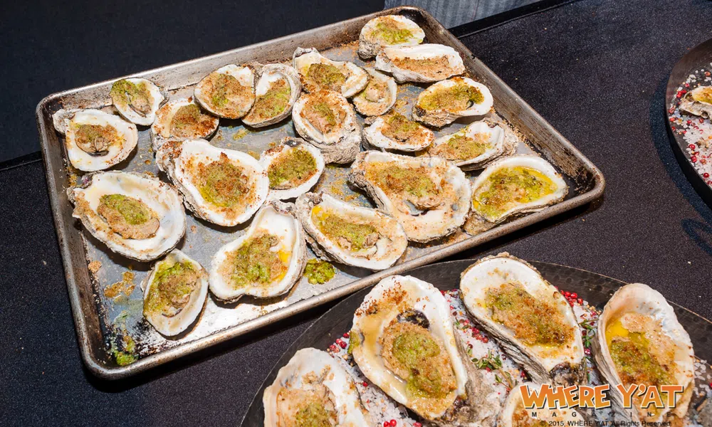 Tray of baked oysters topped with green seasoning and spices served on a black table surface.