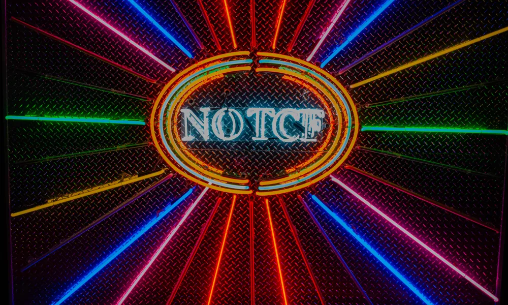 Colorful neon lights radiate from a central oval with the word NOTCF on a textured metal background.