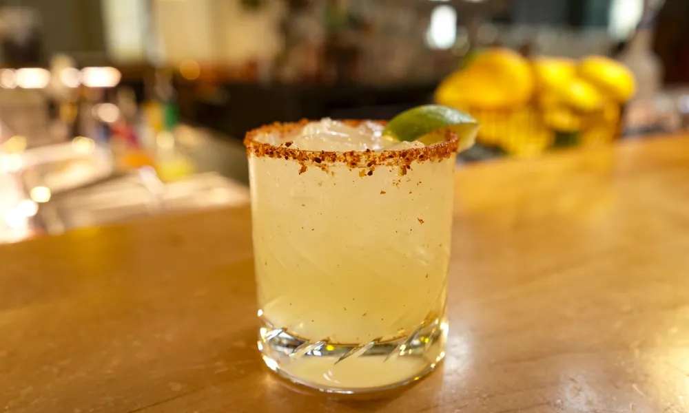 Chilled margarita cocktail with salted rim and lime wedge on wooden bar counter.