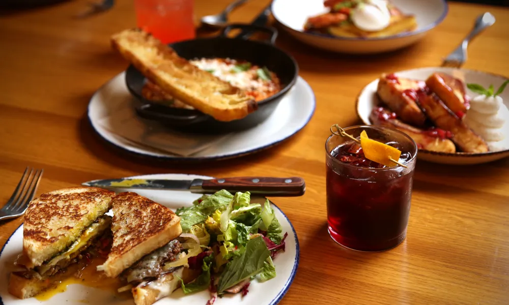 Delicious dishes including a sandwich, salad, drinks, and desserts arranged on a wooden table.