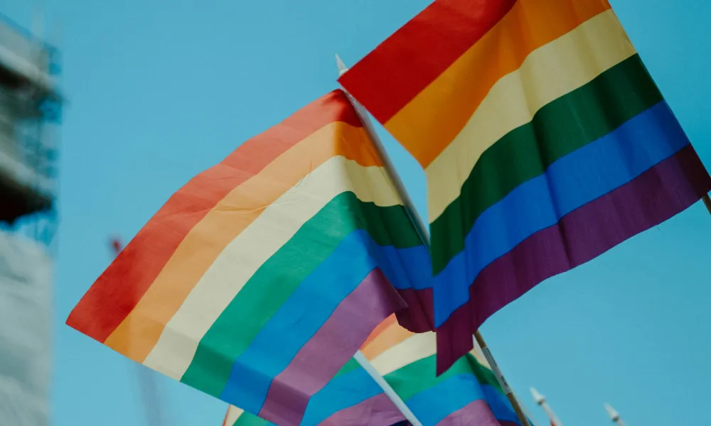 Multiple rainbow pride flags waving against a clear blue sky symbolizing LGBTQ+ pride and equality.