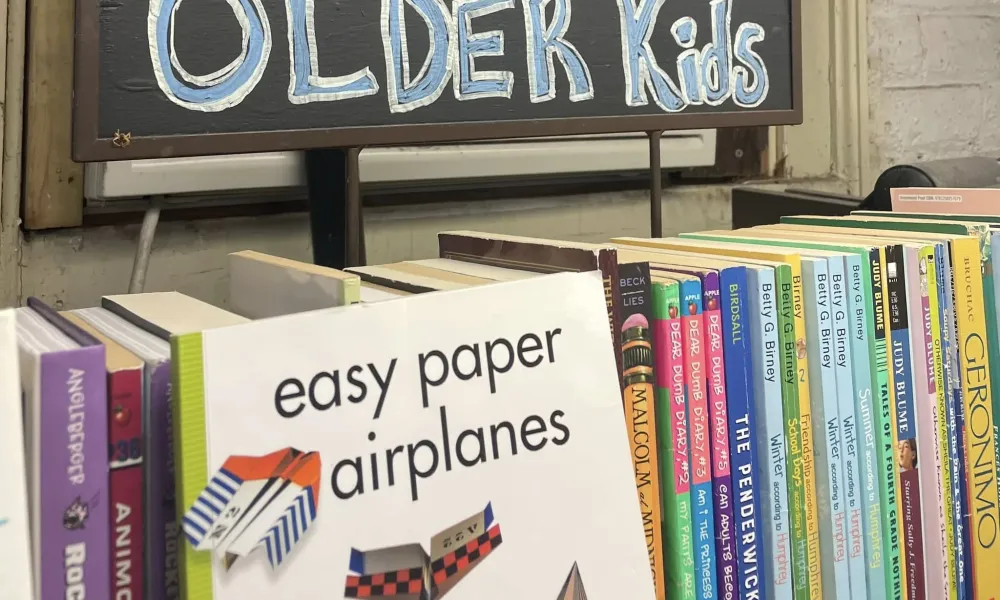 Books for older kids displayed on a shelf with a sign reading Older Kids and a book about easy paper airplanes.