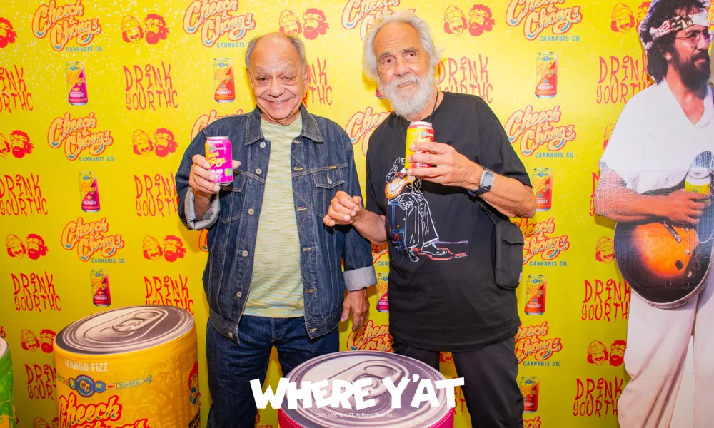 Two men smiling and holding cans of Cheech & Chong's cannabis drink in front of a branded yellow backdrop.