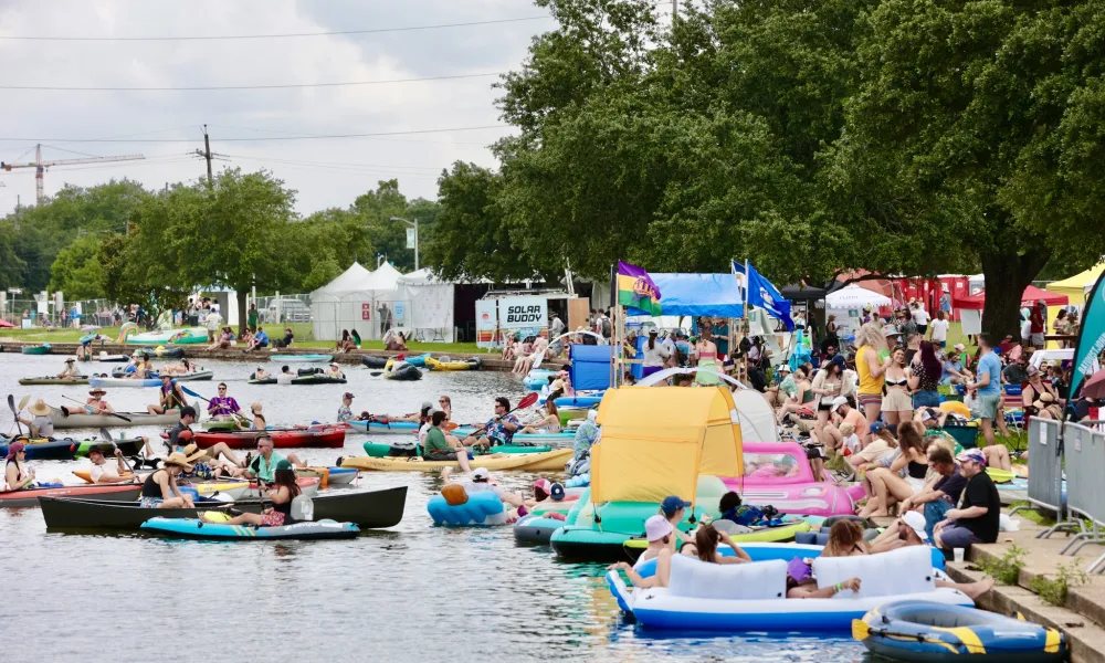 Crowd enjoying a summer festival by the water with kayaks and colorful inflatables.