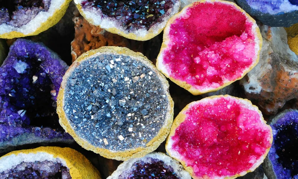 Close-up of colorful geode crystals in shades of purple, blue, pink, and black with rough outer shells.