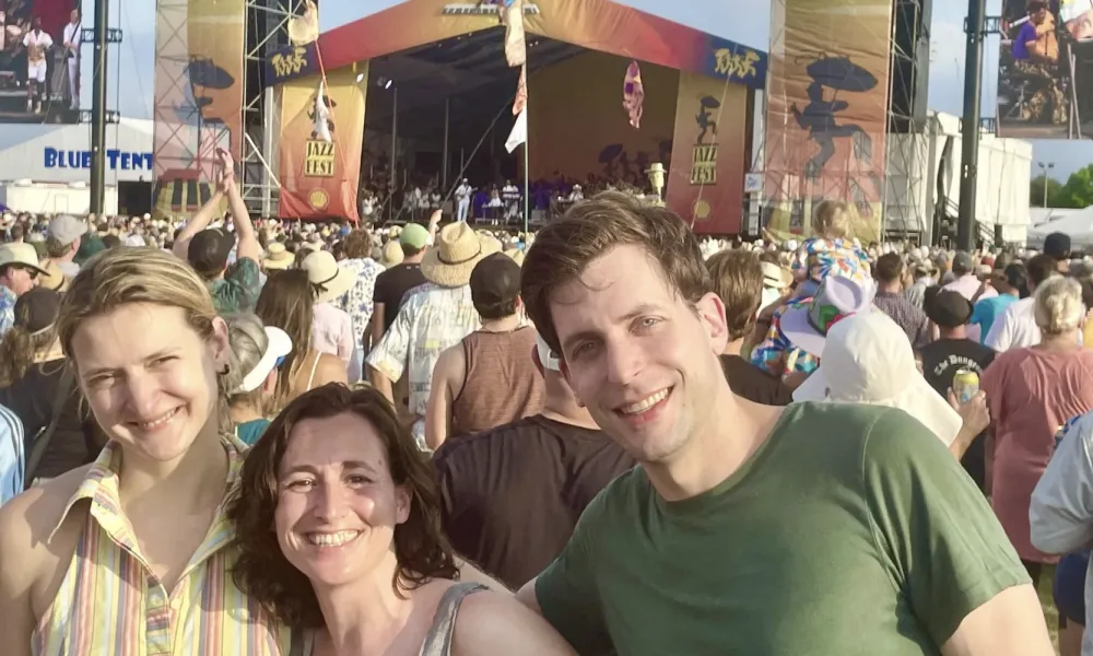 Happy friends smiling at an outdoor music festival with a large crowd and stage in the background