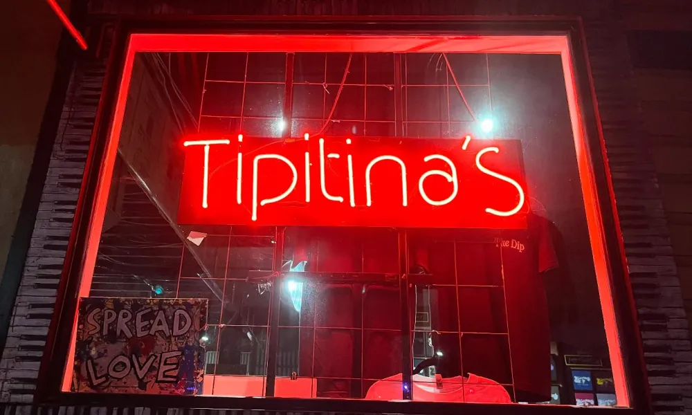 Red neon sign displaying Tipitina's in a window with a Spread Love sign nearby at night.