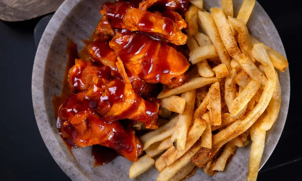 Plate of barbecue chicken wings and seasoned French fries on a gray dish with dark background.