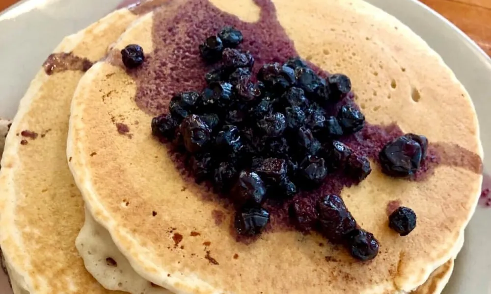 Stack of golden brown pancakes topped with juicy cooked blueberries and blueberry syrup on a plate.