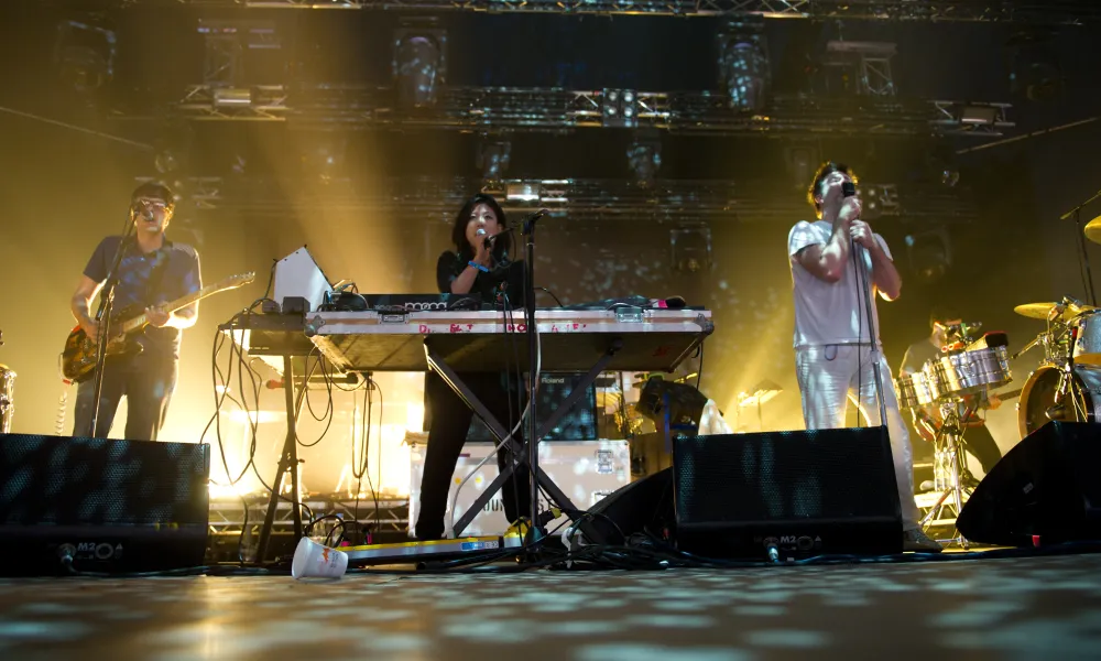 A live performance with musicians on stage, illuminated by vibrant stage lights and a lively crowd atmosphere.