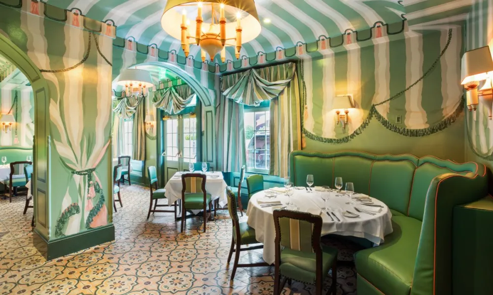 Elegant dining room with green striped walls, round tables with white tablecloths, and vintage-style chairs.