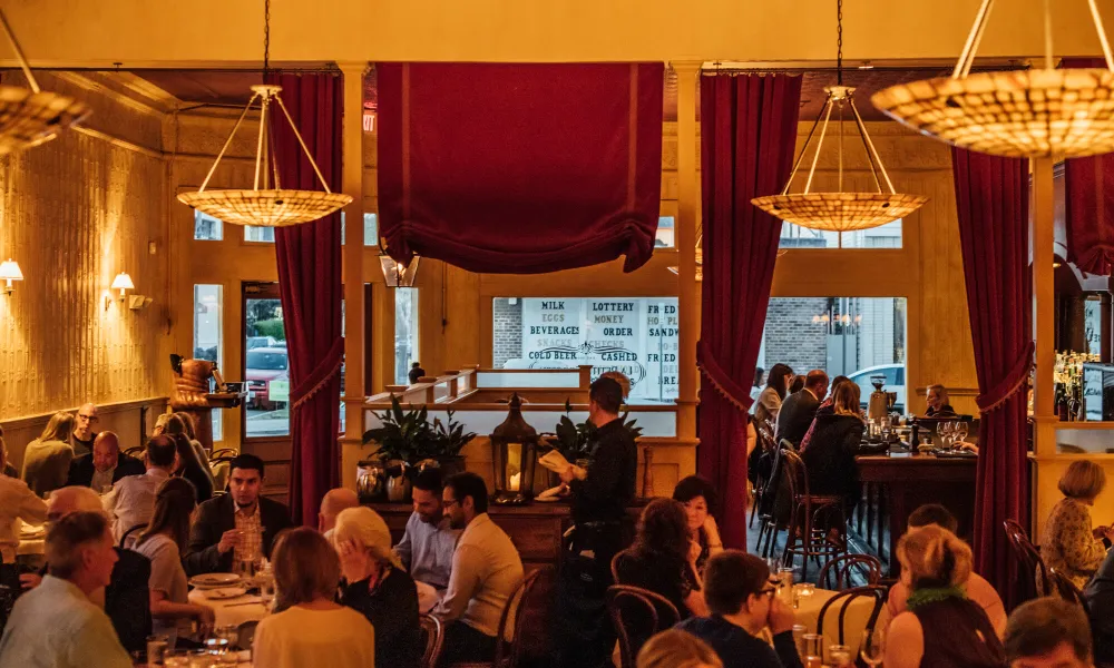 Warmly lit restaurant interior with patrons dining and a waiter serving in an elegant, cozy setting.