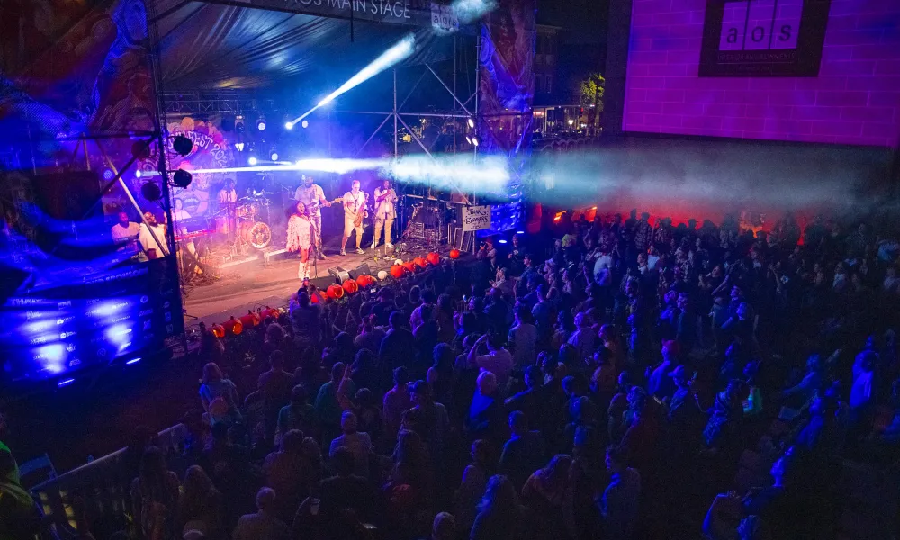 Live band performing on AOS Main Stage with colorful lights and large crowd at night concert event.