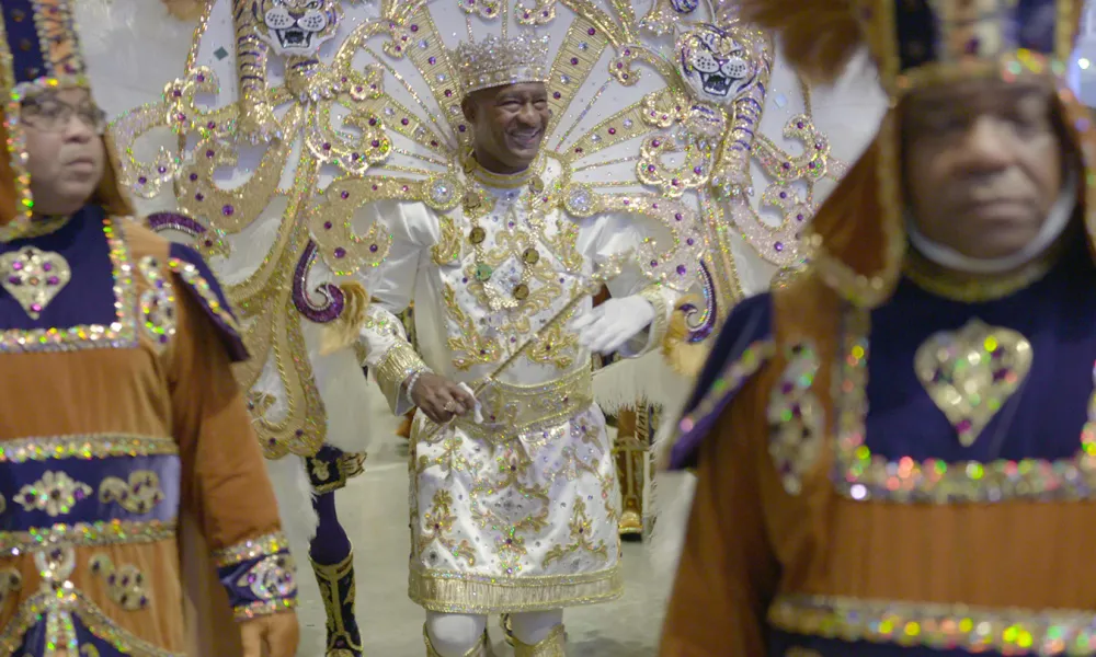 Group of men in vibrant, ornate costumes with gold, white, and purple details at a festive parade