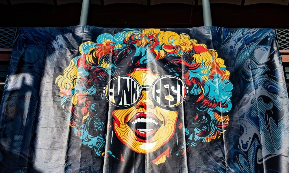 Colorful mural of a smiling woman with curly hair and round sunglasses reflecting bold text on a dark background.