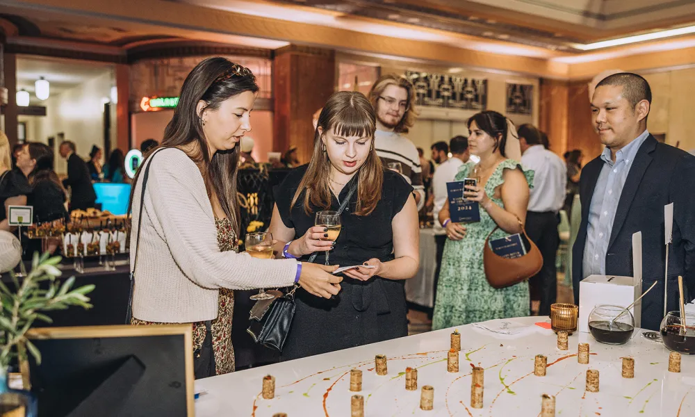 People dressed in semi-formal attire sampling wine and engaging at a social tasting event indoors.