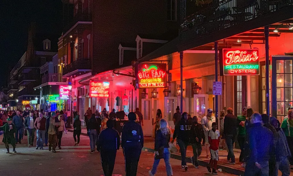 Crowded nightlife scene on a neon-lit street with restaurants and people walking at night.