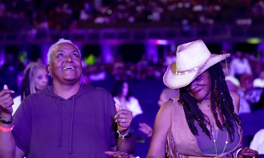 Two women enjoying music, one smiling with eyes closed wearing a cowboy hat, the other with short hair and a hoodie.