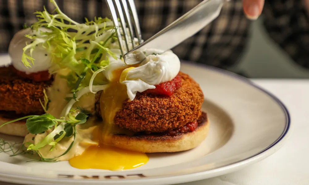 Crispy crab cake Benedict with poached egg, tomato sauce, and fresh salad on a white plate with blue rim.
