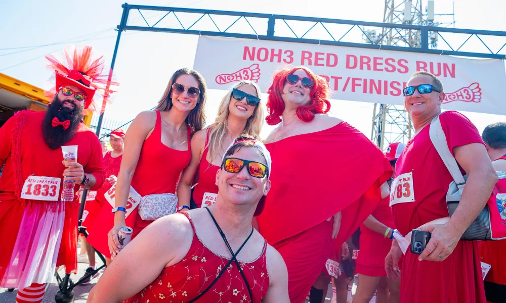 Group of runners dressed in red participating in NOH3 Red Dress Run posing at the start/finish line during daytime.