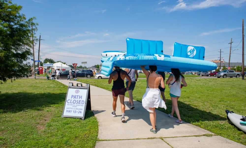 Group carrying large blue float at summer event with a closed path sign in the background.