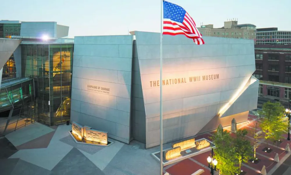 Exterior view of The National WWII Museum with an American flag waving in front during dusk.