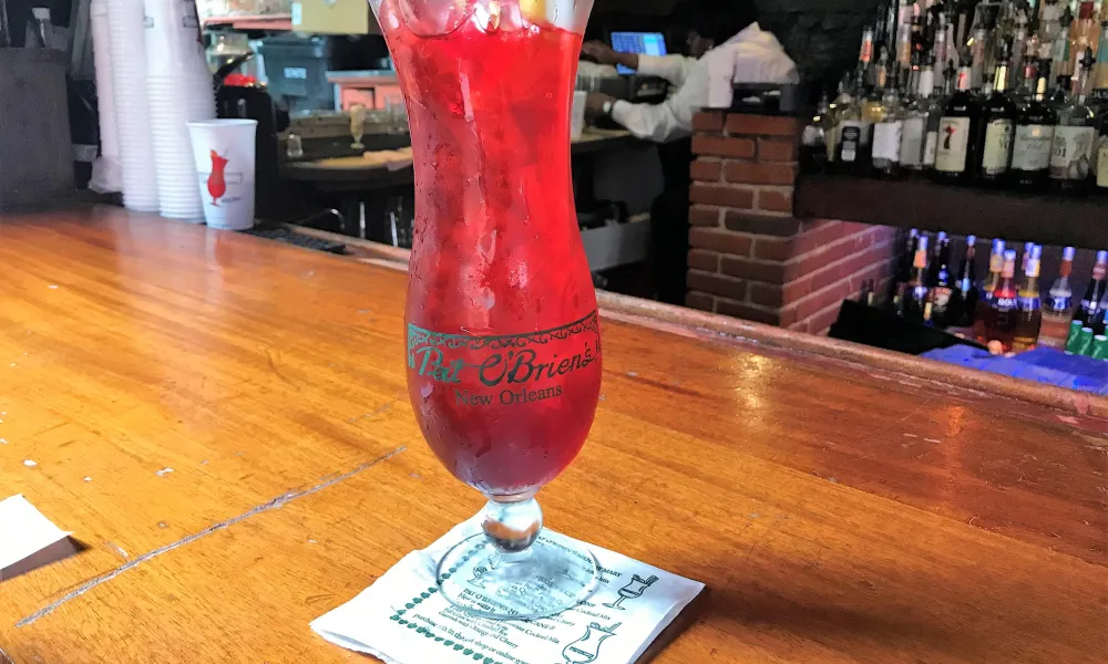 Red cocktail with garnish served in a tall glass on a wooden bar counter at T-Ba O'Brien's New Orleans.