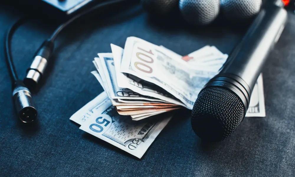 Microphones and audio cables placed next to a stack of US dollar bills on a dark surface