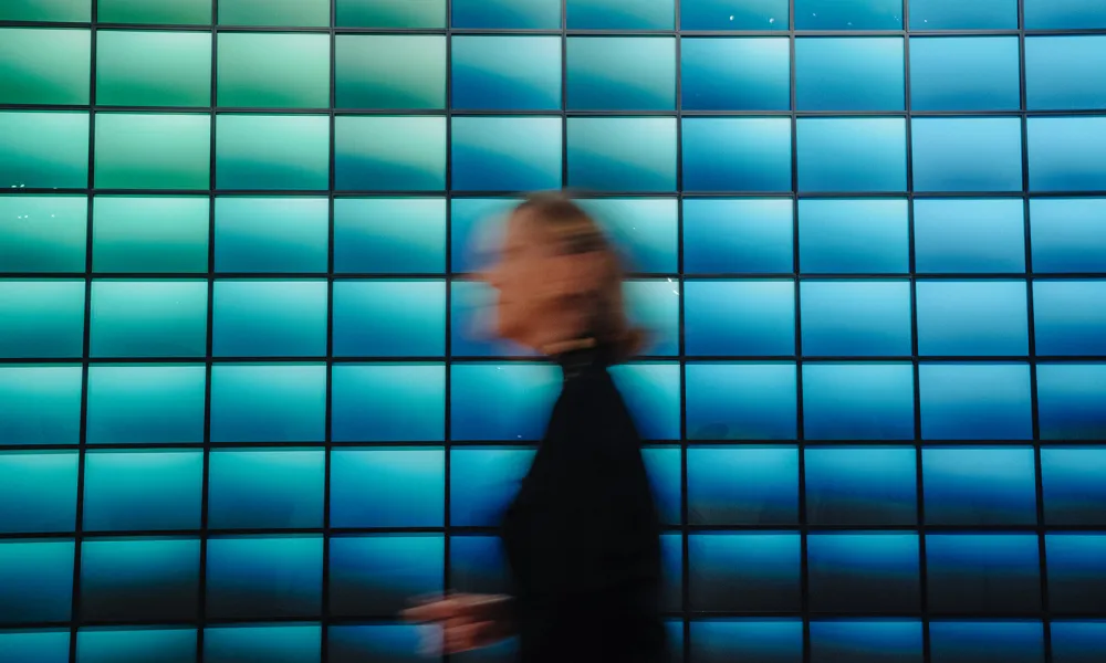 Blurred person walking in front of a vibrant blue tiled wall with gradient lighting