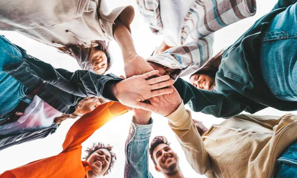 Group of diverse young people standing in a circle with hands joined together in unity and teamwork.
