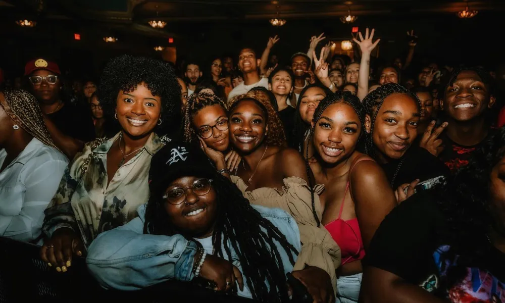 Group of diverse friends smiling and posing closely together at a lively indoor event with warm lighting.