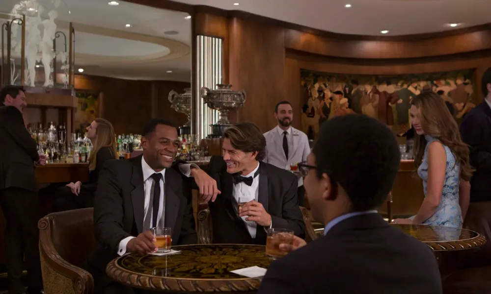 People dressed formally enjoying drinks and conversation at a stylish bar with wood paneling and modern lighting.