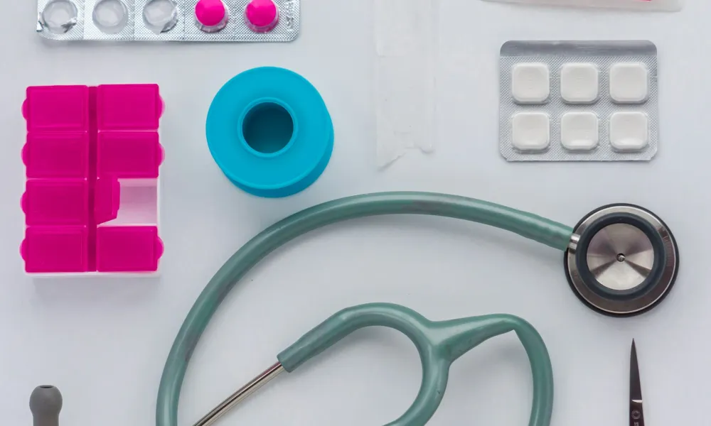 Medical supplies including stethoscope, pill organizer, bandages, tablets, and medical tape on a white surface.