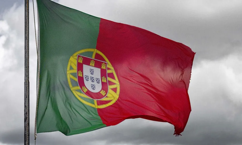 Portuguese national flag waving on a pole against a cloudy sky background