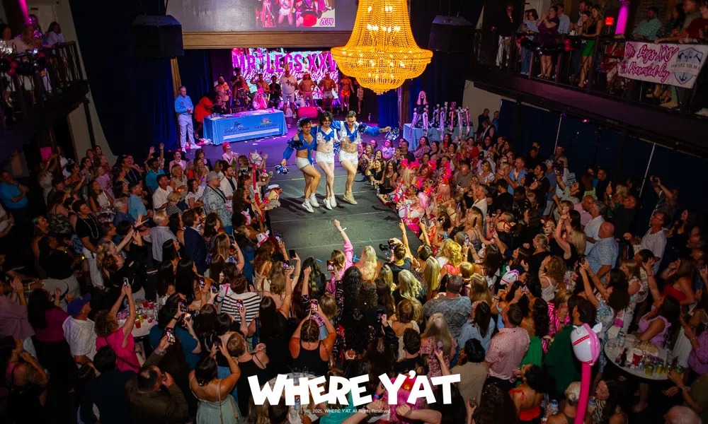 Crowded event with performers dancing on stage under a large chandelier in a vibrant venue packed with an enthusiastic audience.