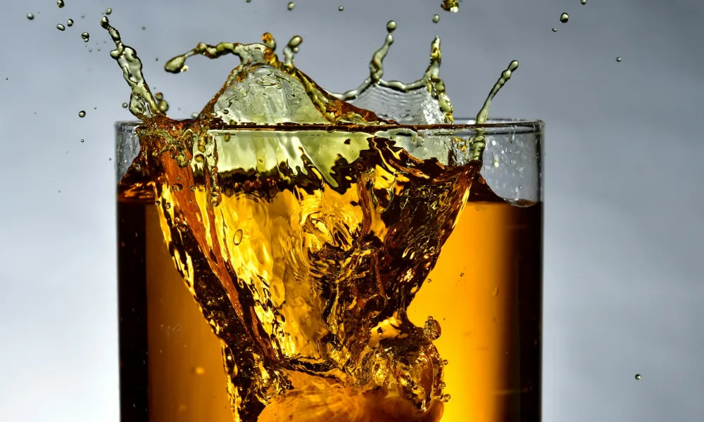 Close-up of a splash in a glass of dark liquid with ice cubes against a gray background